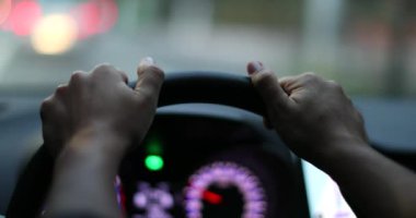 Driver POV holding steering wheel driving in city at night