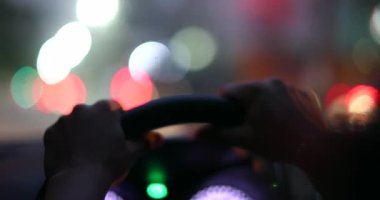 Commuter hands holding steering wheel driving at night in city, waiting in red light POV