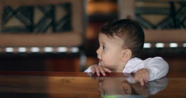 Cute baby holding into table peeking out. Adorable toddler leaning on table