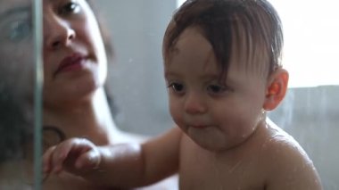 Bathing baby infant inside shower with mother, water splashing in slow-motion