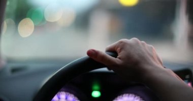Driver point of view, hands holding steering wheel driving in evening in urban city