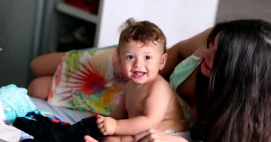 Candid mother and baby together in bedroom bed, casual family moment, young mom with infant child at home