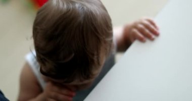 Cute baby toddler learning to stand holding into parent leg, infant one year old development leaning with hand