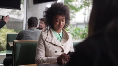 Kahve dükkanında cep telefonu kullanan genç siyah bir kadın. Kafede oturan akıllı telefona bakan Afro-Amerikalı bir kız.
