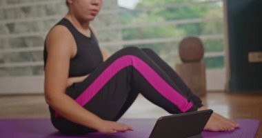 Young girl practicing yoga on mat with online classes via tablet.