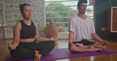 Two friends practicing yoga together in the living room. Man and woman practicing mindful meditation at home