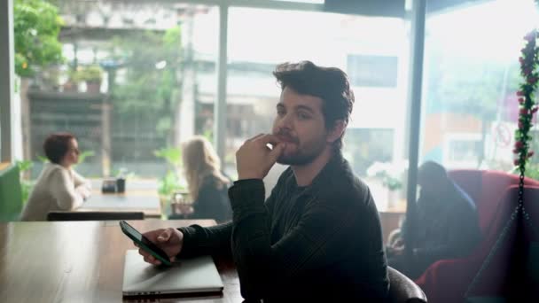 スマホを持った喫茶店に座っている若い男 喫茶店で顎を手に考えている人 — ストック動画