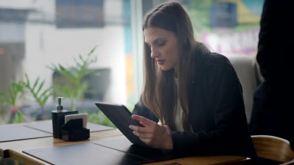 タブレット端末でオンラインでコンテンツを読む喫茶店に座っている若い女性がいた 近代技術を用いて画面に注意を払う者 — ストック動画