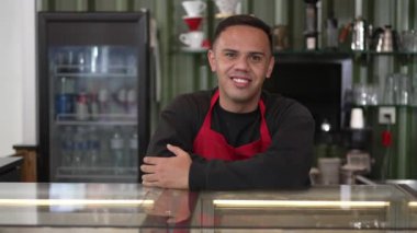 Kahve tezgahının arkasında gülümseyen genç bir Latin Amerikalı barista. Brezilyalı bir iş kafesi çalışanının portresi