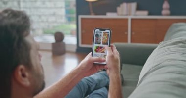 Adam çevrimiçi menüde yiyecek dağıtım uygulamasını tarıyor. Elinde cep telefonu olan biri sipariş için yiyecek kaydırıyor.