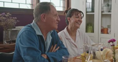 Mutlu bir aile birlikte kahvaltı yapıyor. Yetişkin çocuklarıyla aynı masada oturan orta yaşlı ebeveynler. Genç adam kahvesini yudumluyor ve sohbet dinliyor.