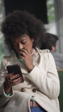 Telefon kullanan siyah bir kadın. Afro saçlı, internetten içerik yiyen Afro-Amerikalı bir kız ciddi bir ifadeyle akıllı telefon ekranına bakıyor.