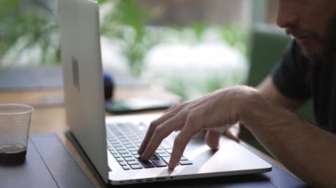 Genç adam kahve dükkanında oturan dizüstü bilgisayarını kullanarak internette geziniyor. Çevrimiçi arama klavyesinde bilgisayar ekranına bakan kişi