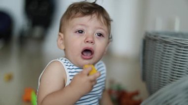 Tearful baby, upset one year old child toddler boy with toy in mouth