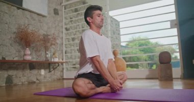 Man stretches on a mat in the living room and practices yoga. He does flexibility exercises and keeps himself fit and healthy.