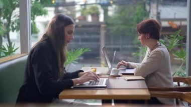 Laptop bilgisayarlarının önünde kahve dükkanında oturan iki genç kadın. Kafedeki teknolojik cihazların önünde çalışan ya da uzaktan çalışan insanlar.