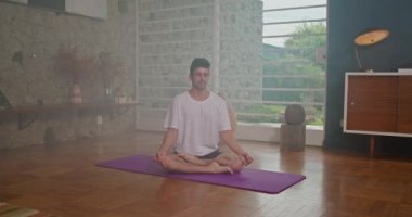 Young man meditating on mat in his living room at home.