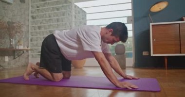 Young man practicing yoga on a mat in living room home interior. Person stretching body