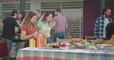 Mutlu aile ve arkadaşlar evlerinin arka bahçesindeki barbeküde. Gençler masada oturup konuşuyor ve içiyorlar..