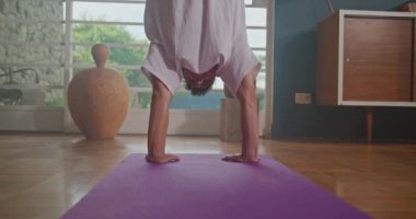 Athlete man balances upside down in yoga practice. Person practicing balance position indoor at living room home. Man doing handstand