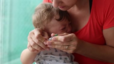 Mother clipping crying baby infant hands. Parent trimming chidl hand naisl. upset toddler