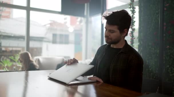 喫茶店でノートパソコンを開く青年 スマホを片付けてカフェでパソコンを使う人 — ストック動画