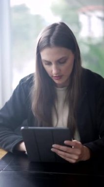 Tablet cihaz ekranına bakan genç bir kadın. Kafede oturan modern teknolojiyi kullanan bin yıllık bir kızın portresi. Dikey video