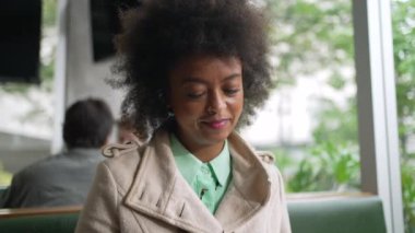 Kahve dükkanında telefonu kontrol eden mutlu bir zenci kadın. Afro saçlı, gülümseyen Afrikalı Amerikalı kız cep telefonu mesajı okuyor.