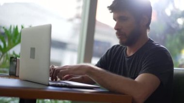 Genç adam kahve dükkanında dizüstü bilgisayar kullanıyor. Kafe restoranındaki bilgisayarda yazan kişi uzaktan çalışıyor..