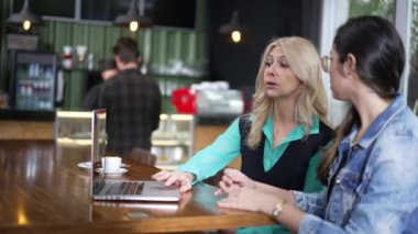 Kahve dükkanında dizüstü bilgisayarın önünde iki kadın. Kafe 'de uzaktan çalışan yeni kadın işçiye üst düzey yönetici yönelimi.