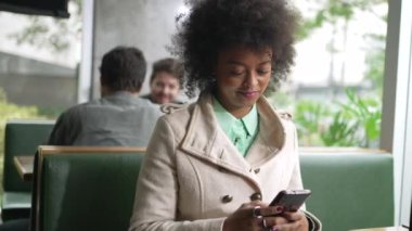 Kafe restoranında telefonu kullanan kişi. Genç zenci Afrikalı Amerikalı bir kadın akıllı telefon ekranına bakıyor.