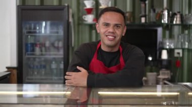 Kahve tezgahının arkasında gülümseyen genç bir Latin Amerikalı barista. Brezilyalı bir iş kafesi çalışanının portresi