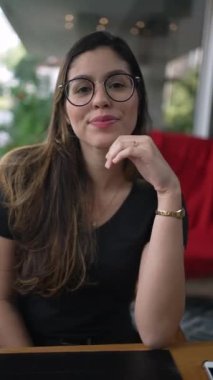 Kahve dükkanında oturmuş kameraya gülümseyen güzel bir genç kadın. 20 'li yaşlarda mutlu bir kız. Dikey Video