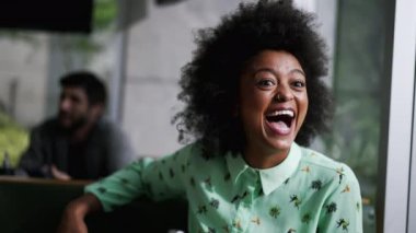 Neşeli Afrikalı Amerikalı kadın kahve dükkanında oturmuş kahkahalarla gülüyor..