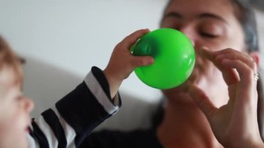 Mother playing with child, mom deflating balloon to baby face teasing