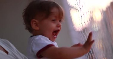 Happy baby touching safety net at balcony. Ecstatic one year old infant child