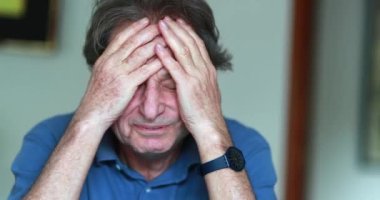 Older man covering face with hands, stressed and tired senior man in 70s feeling pressure