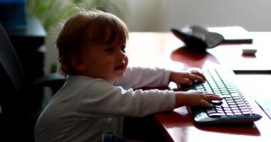 Baby at computer desk pretending work typing on keybaord. One year old child at office