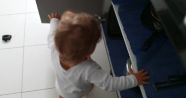 Baby opening kitchen closet grabbing utensils