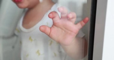 Crying baby leaning on window wanting to get out. One year old hand on glass wanting to exit, in quarantine