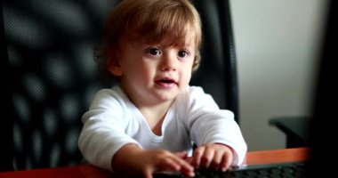 Baby at home office pretending to work in front of computer desk. One year old toddler child
