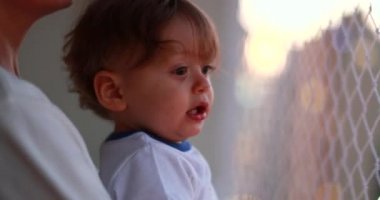 Parent holding one year old infant baby at apartment balcony with safety net