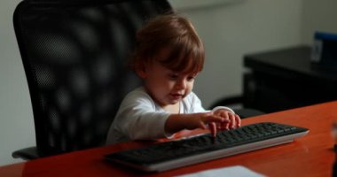 Baby sitting at office desk typing on keyboard computer. Toddler child at work
