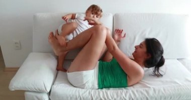 Mom and baby toddler on home sofa together, parent and infant lying down on couch