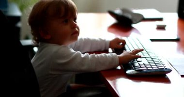Baby at computer desk pretending work typing on keybaord. One year old child at office