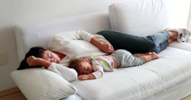 Candid mother sleeping together lying in sofa. Authentic exhausted parent with baby