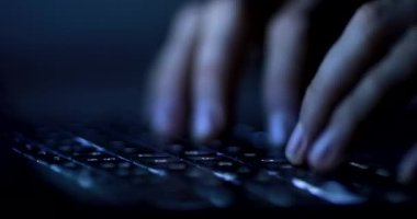 Hands typing on computer keyboard at night, close-up of person writing on laptop keyboard