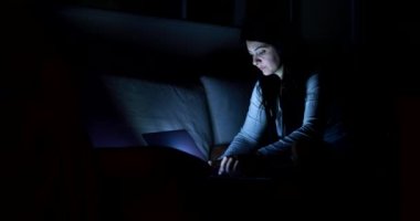 Woman browsing internet on laptop screen at night in living-room alone