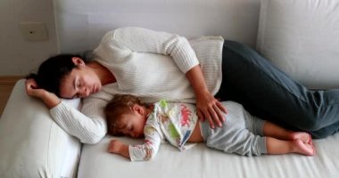 Tired mom and baby napping lying in couch. Mother and infant sleeping together