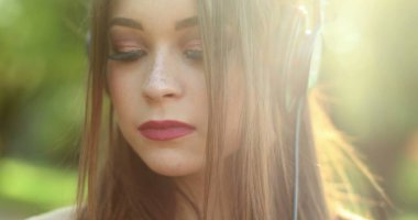 Millennial girl enjoying music, song, podcast, or audiobook in outdoor park. Woman holding cellphone with headphones